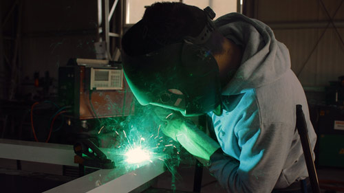 Image of an ironworker engaging in his profession using welding tool, and necessary protective gear, depicting the most essential tools of an ironworker