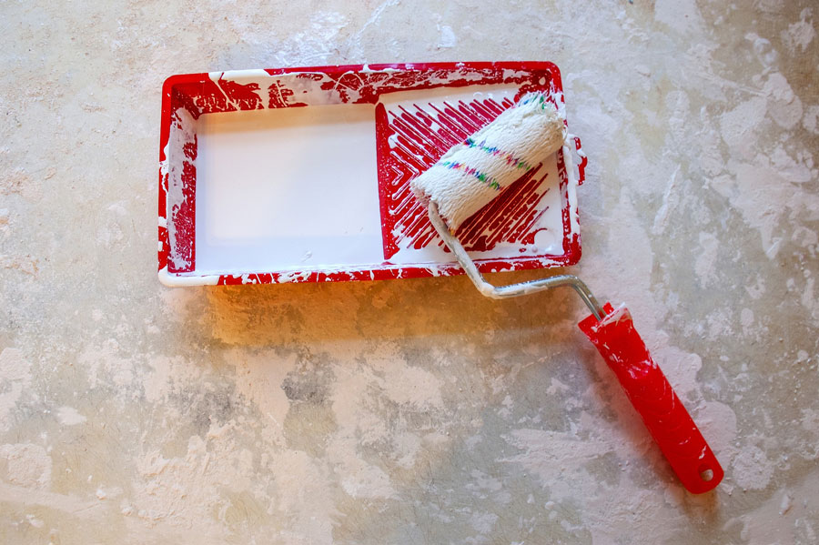 A picture of a roller brush and a paint tray depicting the tools of a house painter