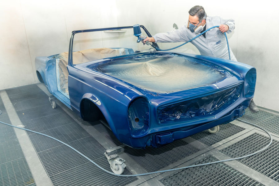 Image of an auto painter painting a car using a spray painter