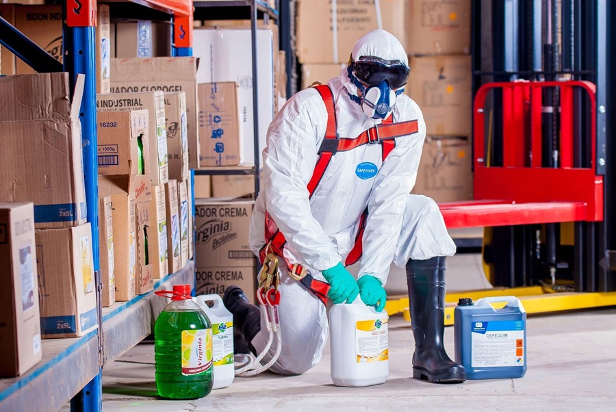 A hazmat removal worker wearing personal protective equipment including eye protection, a face mask, and a harness who is about to use chemicals for hazmat removal