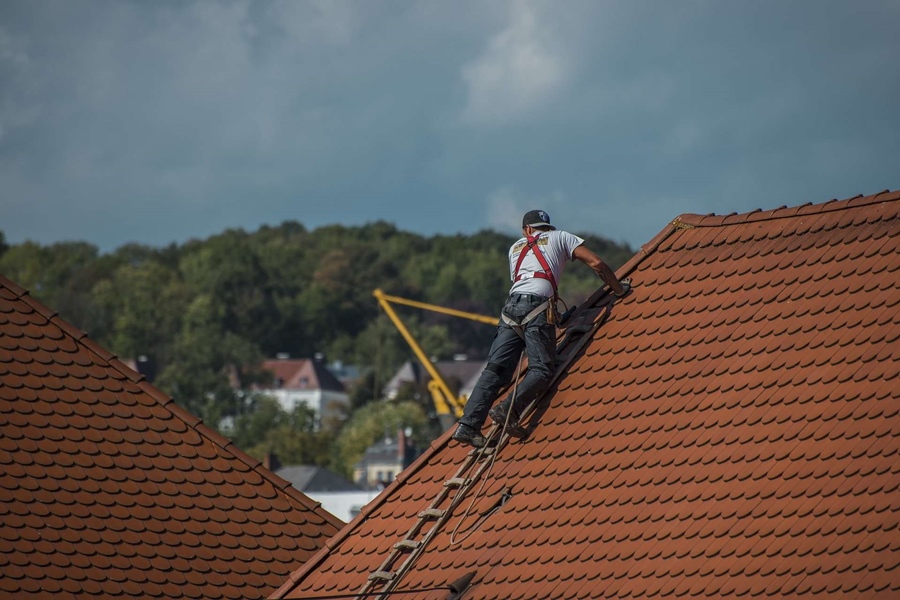 A roofer working on a roofing project with a ladder wearing all the personal protective equipment in a countryside