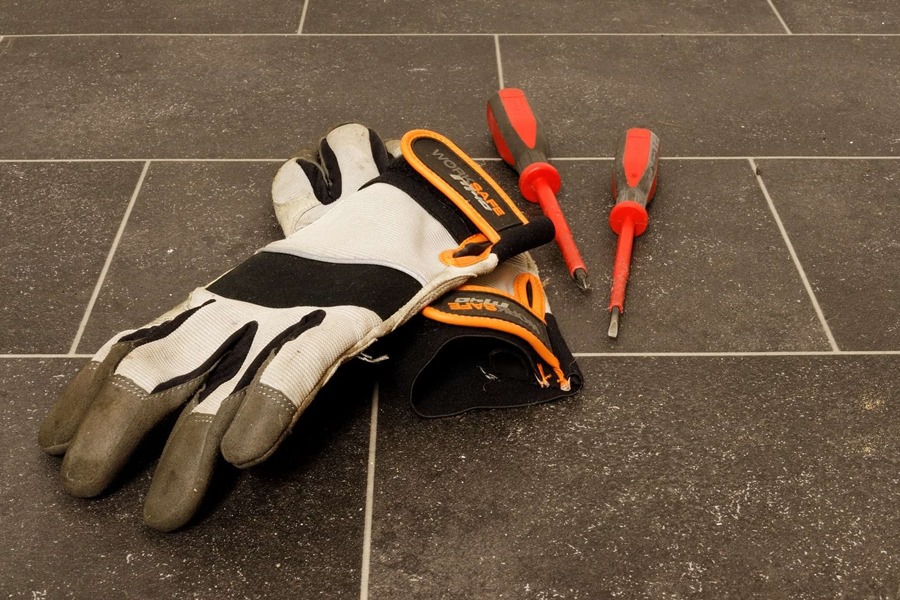 A pair of insulator gloves and two screwdrivers on a tiled floor depicting the tools of an insulation worker